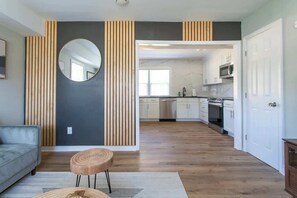 A modern kitchen with white cabinets, a microwave, and a dishwasher. There is a round mirror on the wall and a wooden floor. - Group Stay • 2 Spacious Homes near Downtown & Park (Raleigh)