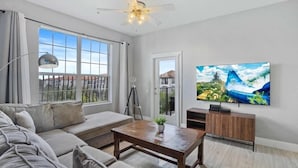 Ein modernes Wohnzimmer mit großem Fenster, Deckenventilator, Flachbildfernseher und Sofa.