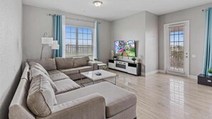 A modern living room with a sectional sofa, a flat-screen TV, a coffee table, and a sliding door. - Spacious 4BR Vista Cay Retreat near Universal (Orlando)