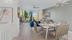 A dining area with a modern chandelier, a dining table set for four, and a view of the outdoors through large windows. - Vista Cay 3BR Condo near Universal (Orlando)