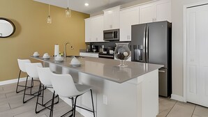 A modern kitchen with white cabinets, a black refrigerator, and a central island with bar stools. - 4BR Storey Lake Home, Sleeps 10 (Kissimmee)
