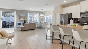 Een ruime keuken met witte kasten, een centraal eiland met barkrukken, en een zithoek met een bank en stoelen.