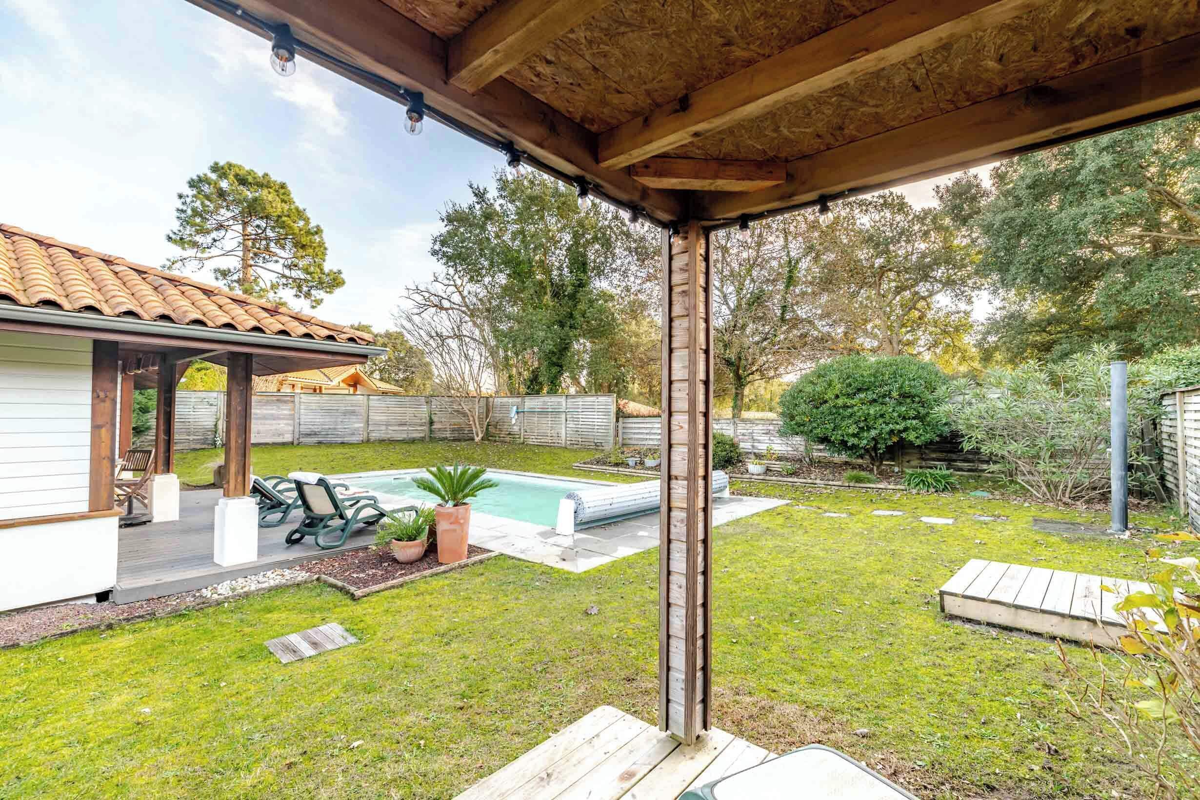 Ein Garten mit Holzterrasse, Schwimmbecken und überdachter Terrasse.