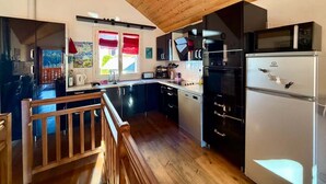 Eine kleine Küche mit Holzbalkendecke, einem Kühlschrank und einem Fenster mit roten Vorhängen.