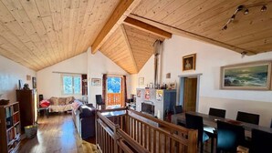 Ein geräumiger Wohnbereich mit Holzboden, hoher Decke und einem Essbereich mit langem Tisch und Stühlen.