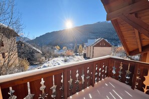 A wooden balcony with decorative metal railings overlooking a snowy village with houses and mountains in the background. - Charming and bright cottage in Briançon (Briançon)