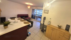 A modern kitchen with a dining area, featuring a large island with a sink, a dining table with placemats, and a view of a balcony with a checkered floor. - Comfortable stay in the heart of La Seyne-sur-Mer (La Seyne-sur-Mer)
