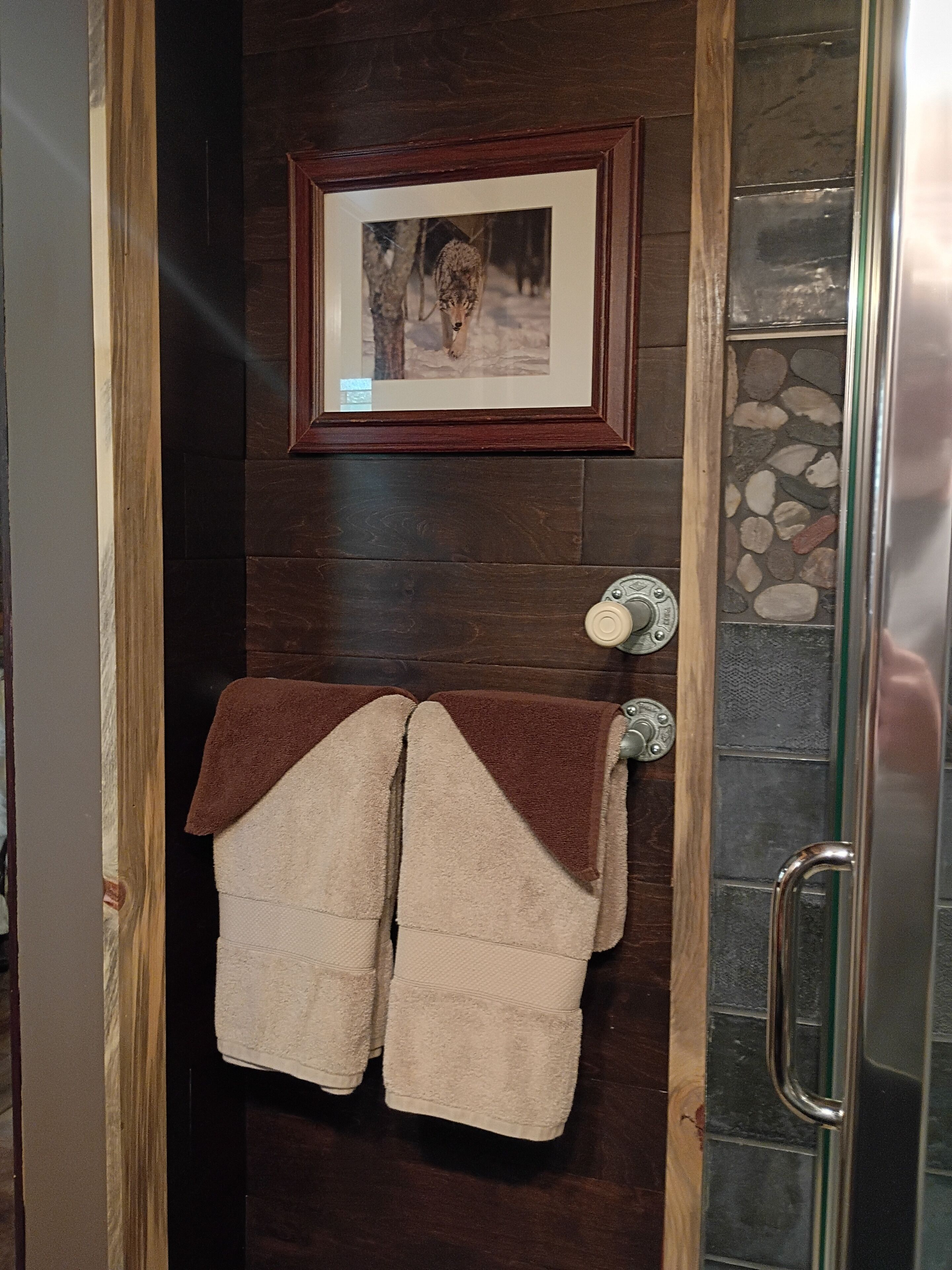 Un bagno con una porta in legno scuro, un quadro incorniciato sopra il porta asciugamani e una parete in pietra a destra.