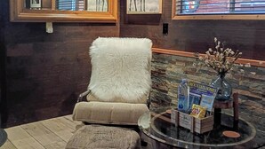 A cozy room with a wooden ceiling, a large mirror, framed deer pictures, a plush armchair, a wicker ottoman, and a wooden barrel table with a vase and a Mountain Homes brochure. - Cozy modern rustic 1-bedroom studio in Idyllwild.  Perfect hideout close to town (Idyllwild-Pine Cove)