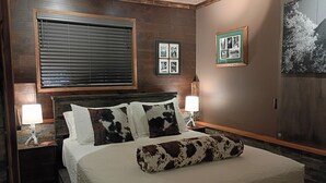 A bedroom with a large bed, wooden headboard, two bedside tables with lamps, a window with blinds, and framed pictures on the wall. - Cozy modern rustic 1-bedroom studio in Idyllwild.  Perfect hideout close to town (Idyllwild-Pine Cove)