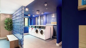 A modern laundry room with a blue and white color scheme, featuring a bench, a washing machine, and a dryer. - Student Only Hollis Wharf (Bath)