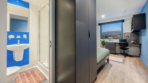 Quarto moderno com cama, escrivaninha e janela com vista para a paisagem urbana.