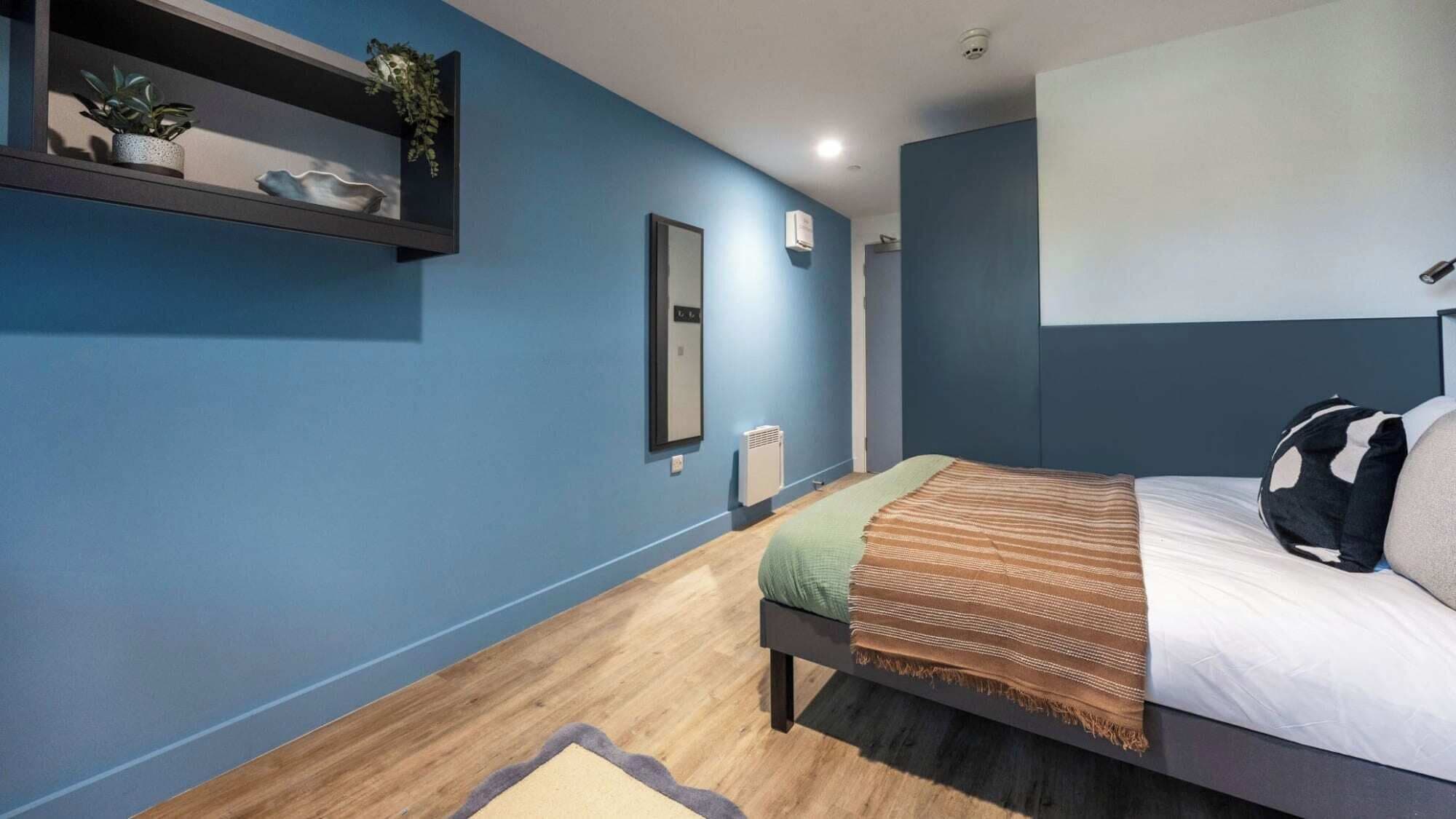 A modern bedroom with a bed, a bedside table, a mirror, and a shelf with decorative items.