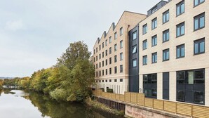 A modern building with multiple windows and a river in the background. - Student Only Hollis Wharf (Bath)