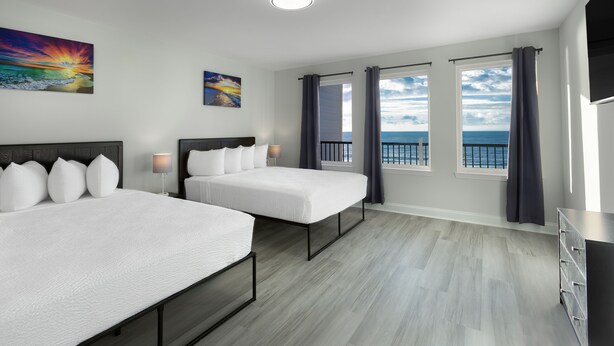 Ett hotellrum med två sängar, ett stort fönster med gardiner, en tavla och utsikt över havet.