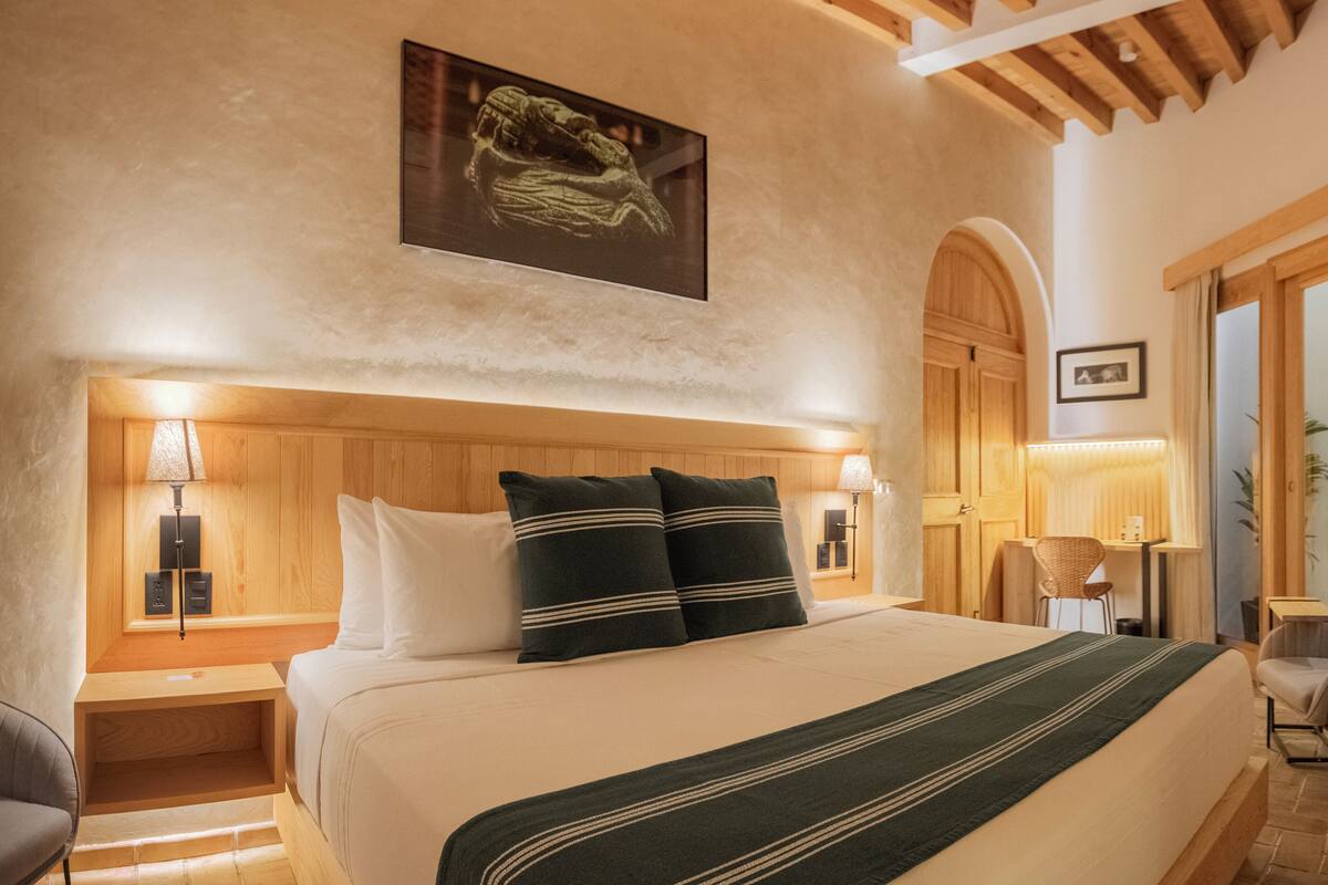 Un dormitorio bien iluminado con una cama grande, cabecera de madera y dos mesitas de noche con lámparas.