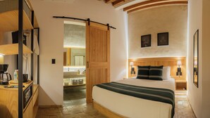 A bedroom with a wooden bed, a nightstand with a lamp, and a bathroom visible through an open door. - Casa Ziña (Oaxaca)