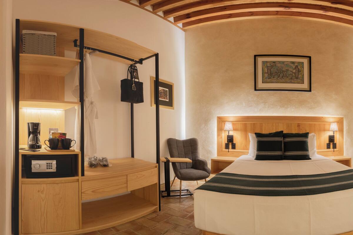 Una habitación de hotel con cama, mesitas de noche, una silla, escritorio y armario.