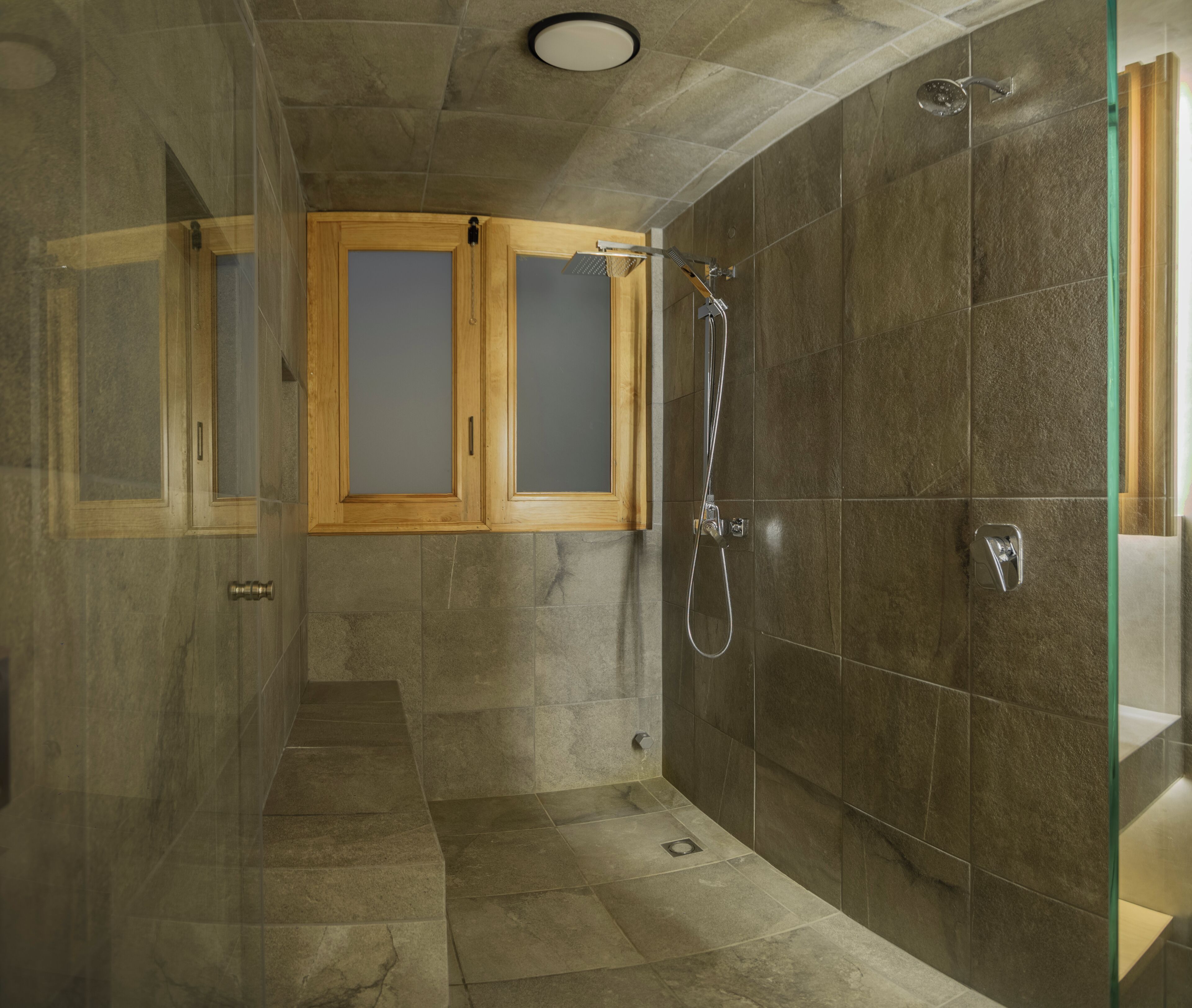 Una doccia con porta in vetro, finestra in legno e soffione.