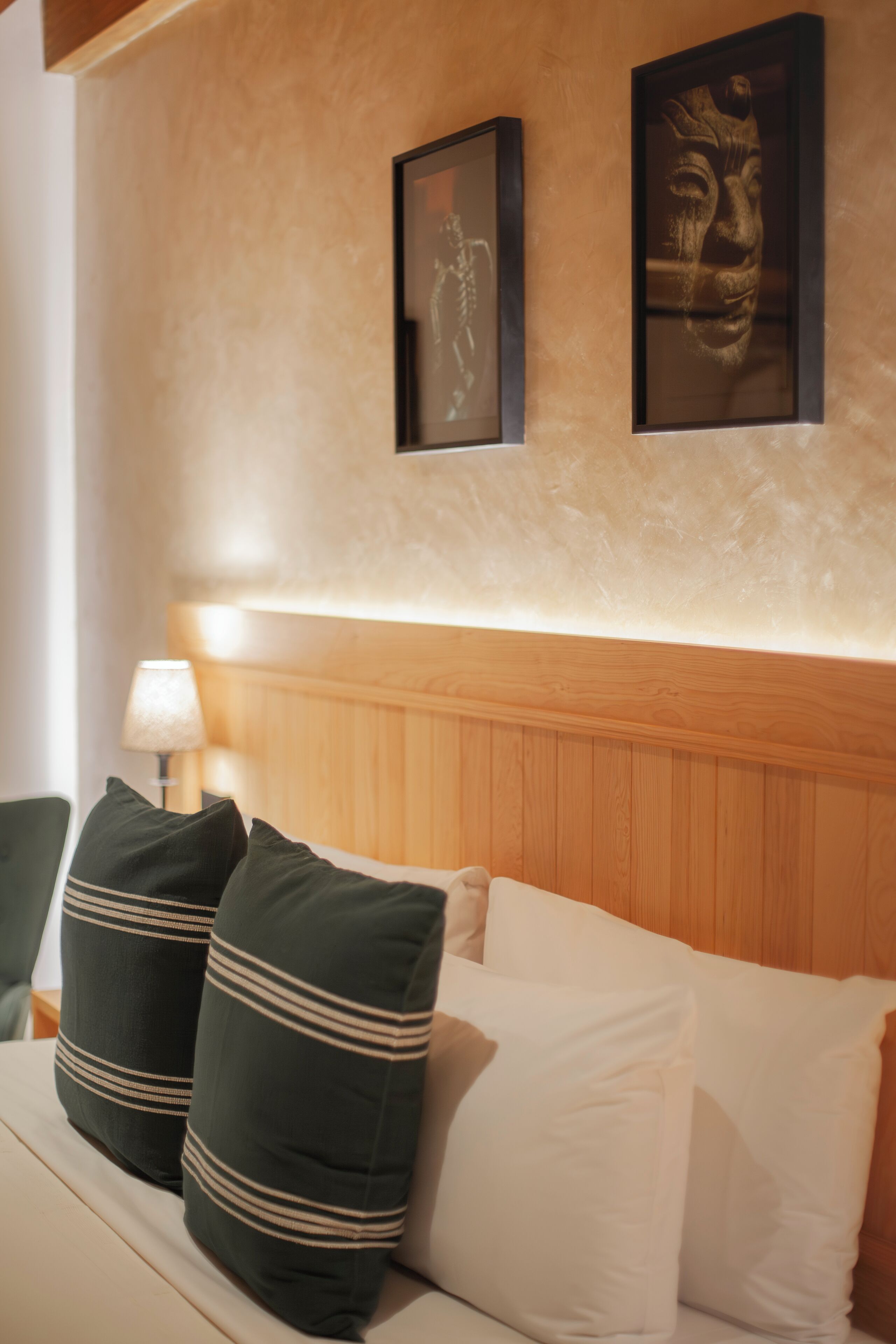 Hotellihuone, jossa on puinen sängynpääty, valko- ja vihreäraidalliset tyynyt sängyllä sekä kaksi kehystettyä taideteosta seinällä.