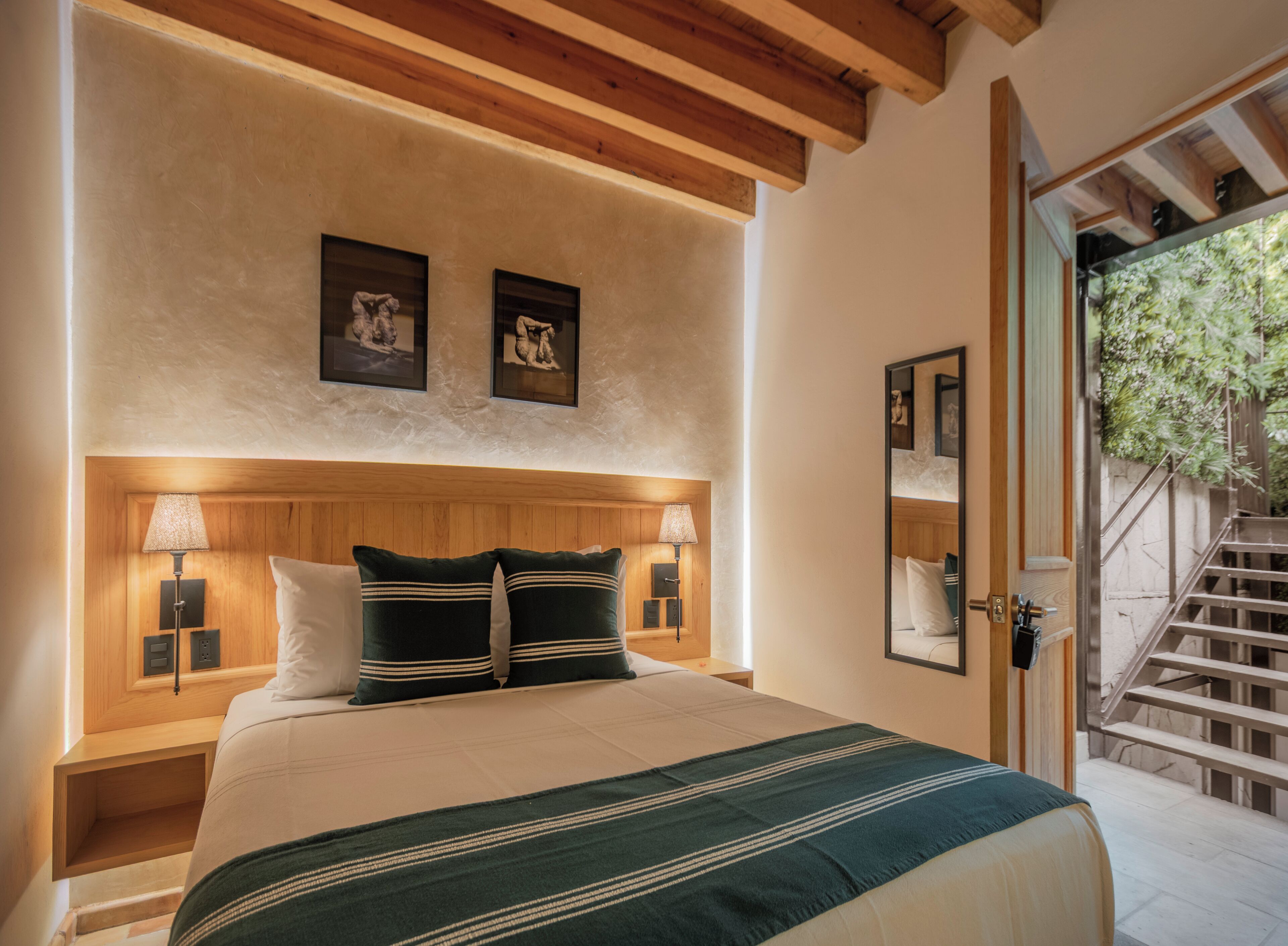 Ein Schlafzimmer mit einem Holzkopfteil, zwei Nachttischlampen, einem Bett mit einer grün gestreiften Decke und zwei gerahmten Bildern an der Wand.