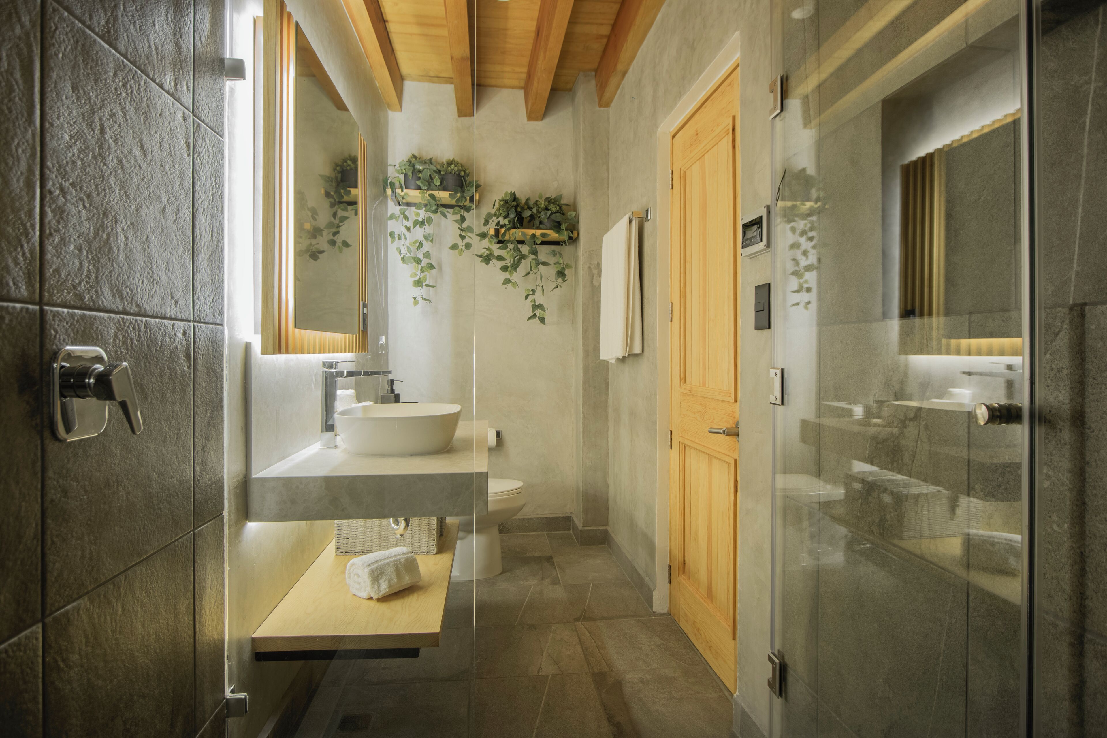A modern bathroom with a stone tile wall, a wooden ceiling, a large mirror, a sink, and a toilet.