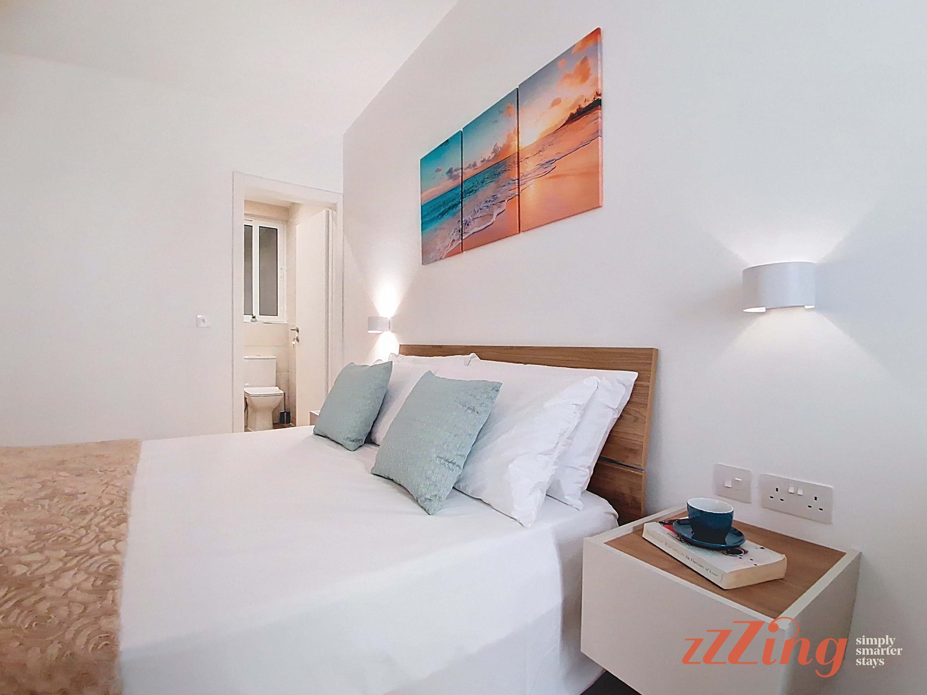 A hotel room with a bed, bedside table, and a wall-mounted painting.