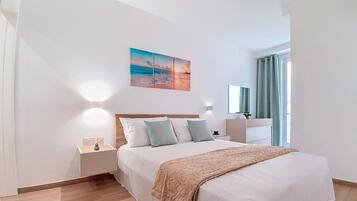 Et moderne hotelværelse med en stor seng, et natbord, en lampe fastgjort til væggen og et maleri af en solnedgang over havet.