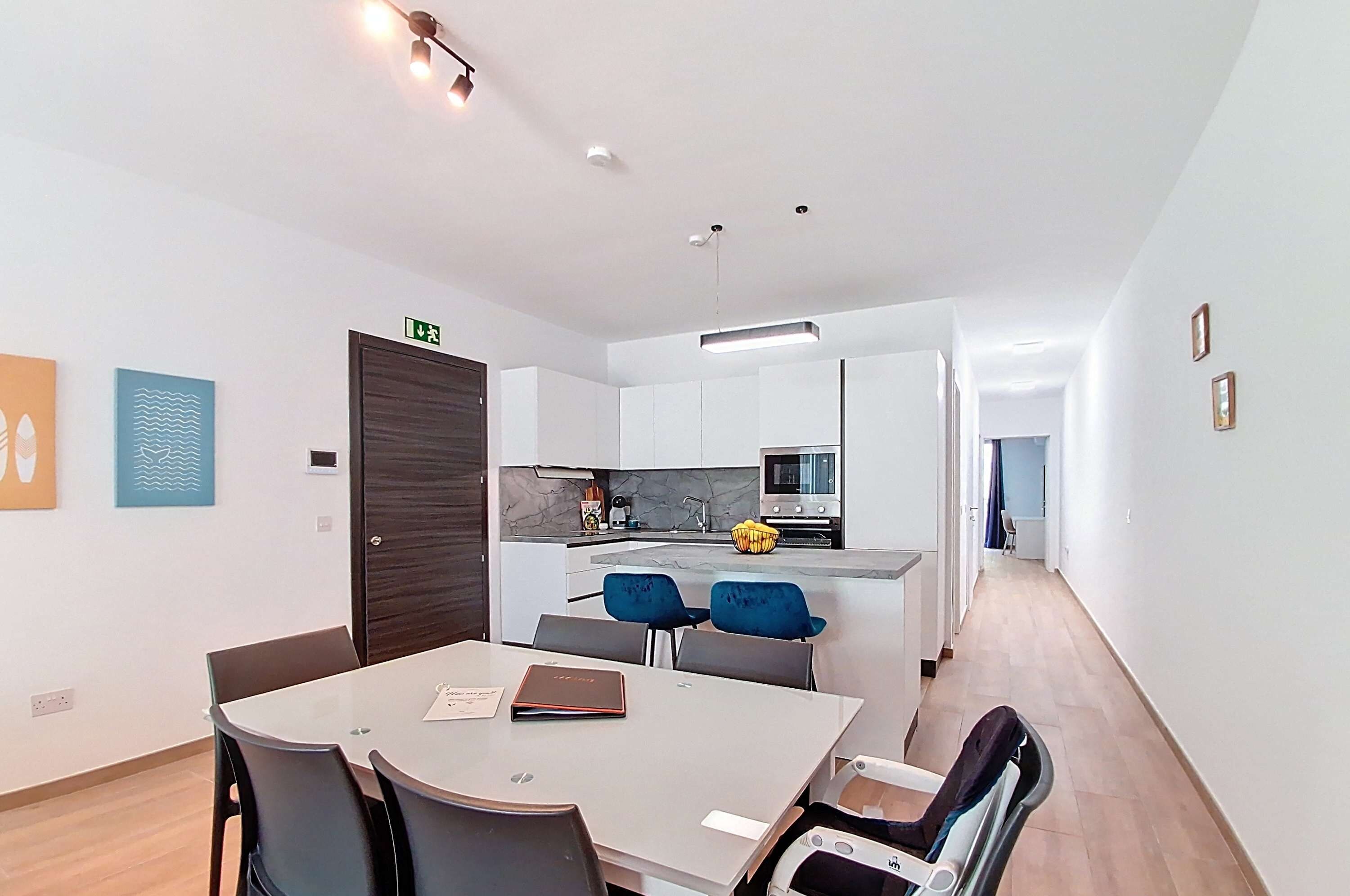 A modern apartment with a dining area, kitchen, and a hallway leading to another room.