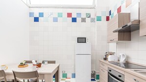 A compact kitchen with a refrigerator, microwave, and a small oven. The floor has a colorful tile pattern, and the walls are tiled with a mix of white and multicolored tiles. - Apartment in Plebiscito int 11 (Napoli)