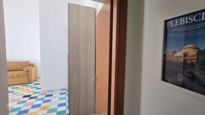 A hotel room with a beige sofa, a colorful checkered floor, and a poster of a historical building. - Apartment in Plebiscito int 11 (Napoli)