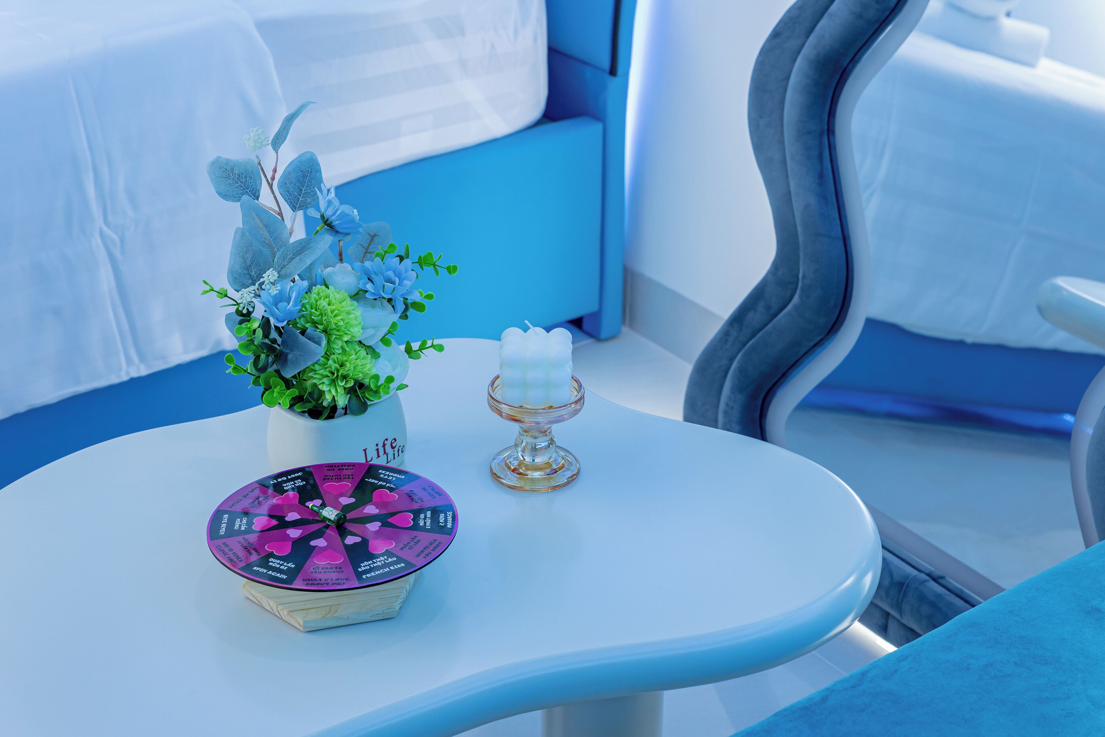 A modern room with a white table, a potted plant, a candle, and a decorative wheel.