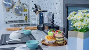 Una cucina moderna con zona pranzo, caratterizzata da un piano di lavoro bianco, diversi utensili da cucina, una macchina da caffè e un vaso decorativo con fiori.