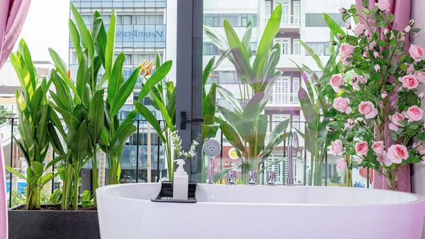 Un bagno moderno con una grande vasca, piante in vaso e vista su un edificio attraverso una finestra.