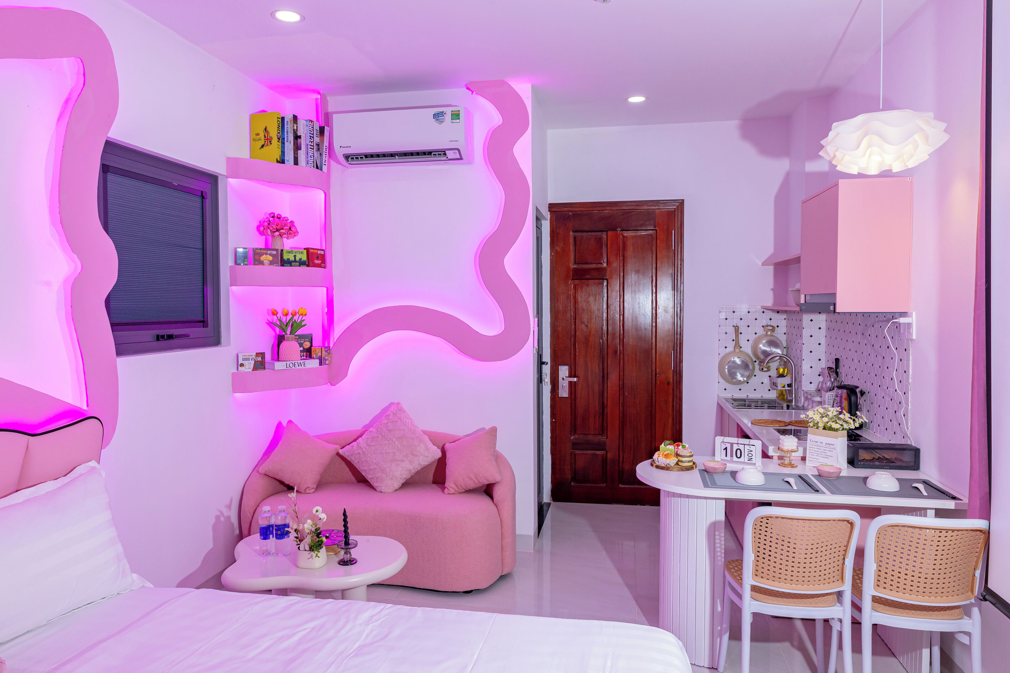 A modern room with a pink sofa, a small round table, and a kitchenette area with a wooden door.