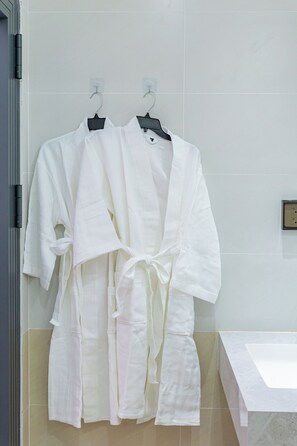 A bathroom with two white robes hanging on a rack, a white sink, and a tiled wall. - ORI HOME (Ho Chi Minh City)
