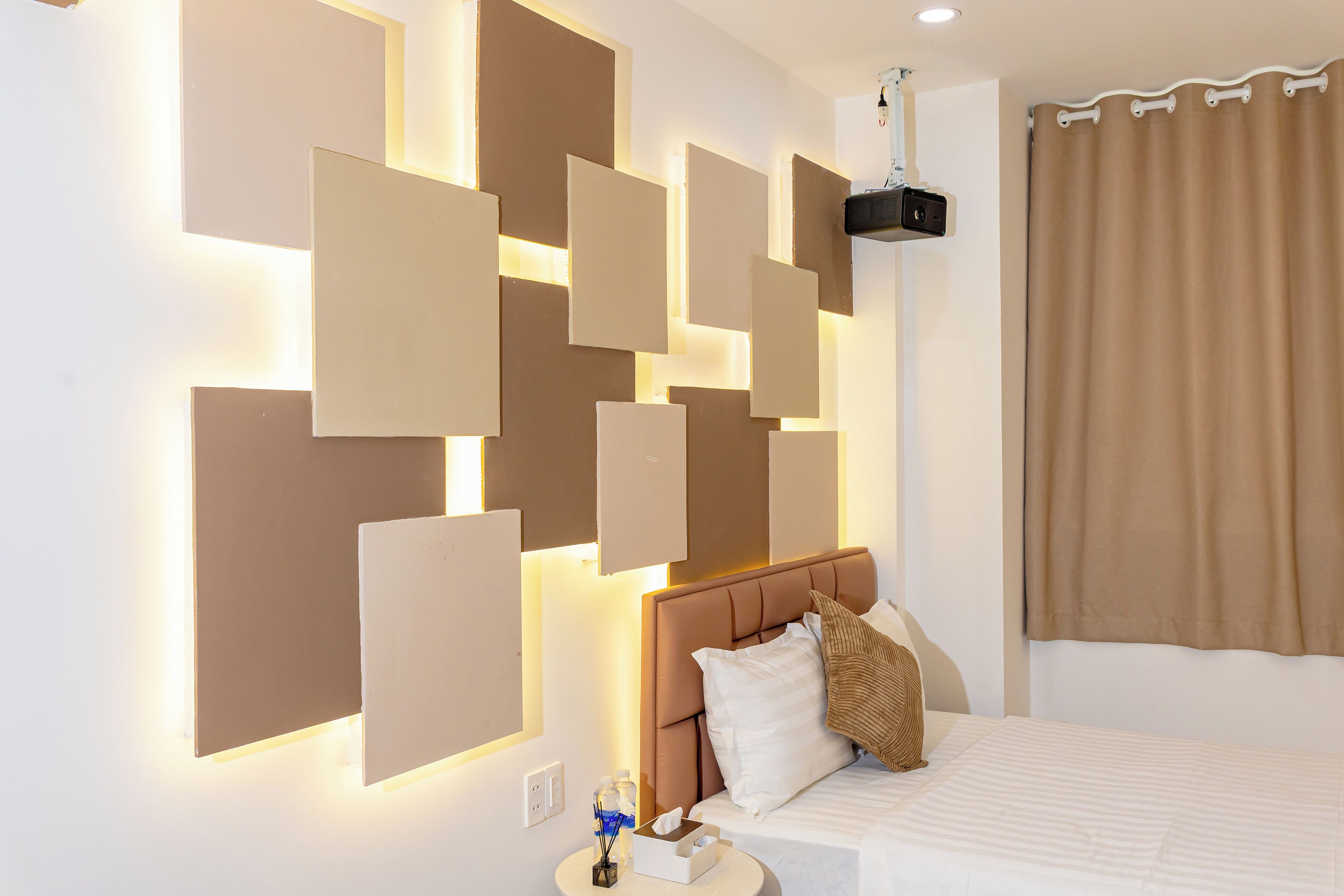 A hotel room with a modern design, featuring a large bed with a headboard, a bedside table with a lamp, and a wall-mounted light panel.