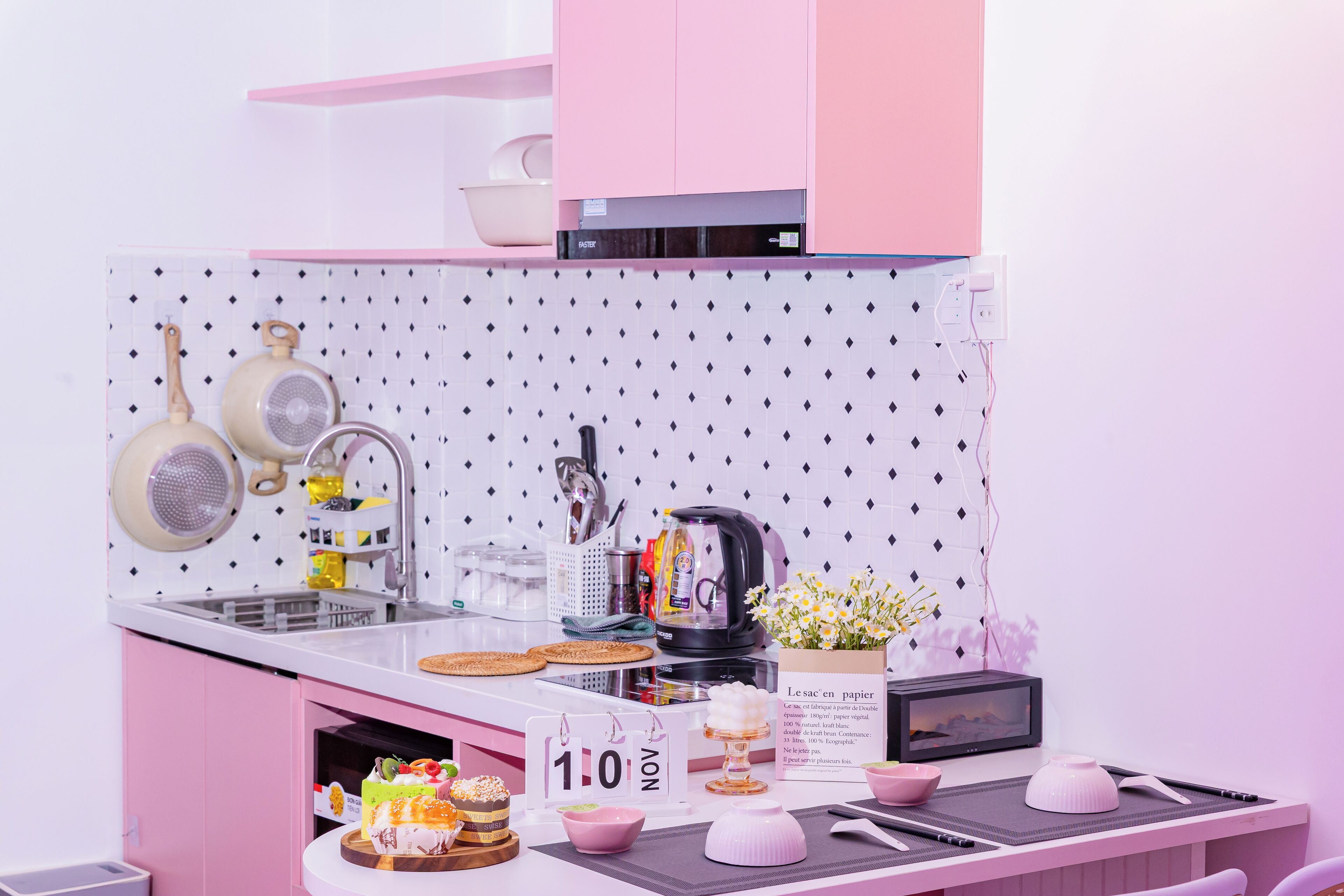 A kitchen with pink cabinets, a white backsplash, and various kitchen appliances and utensils.