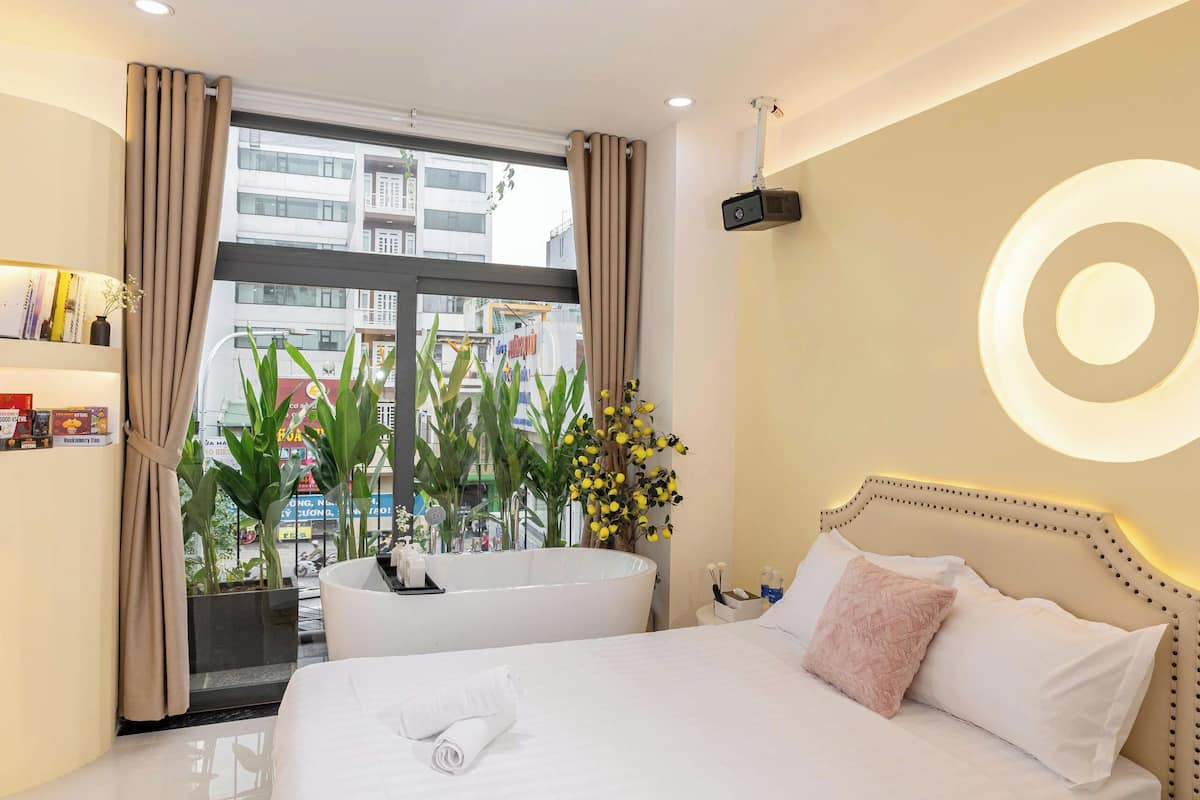 A hotel room with a large bed, a bathtub, and a view of the city through the window.
