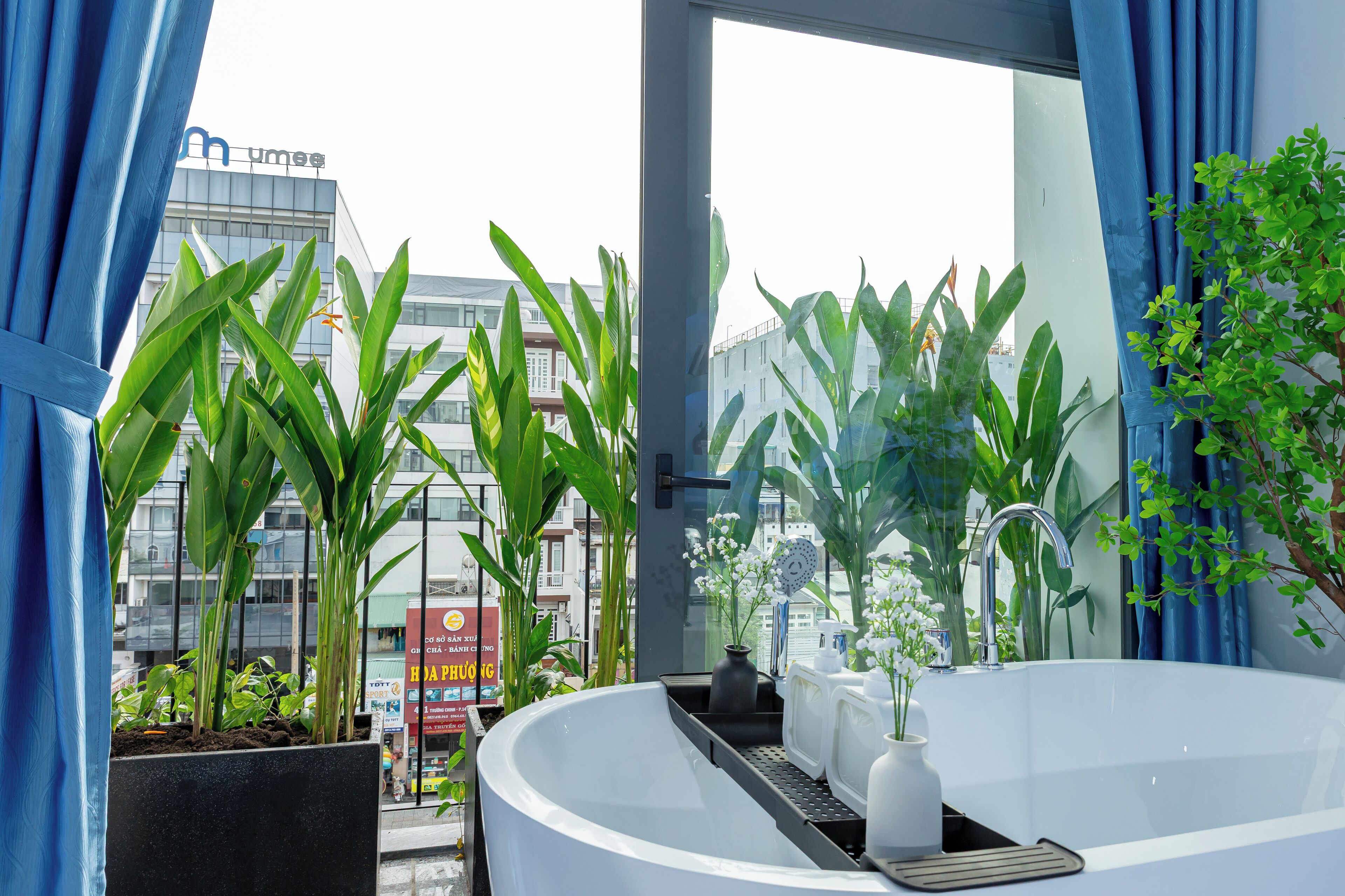 A modern bathroom with a large bathtub, potted plants, and a view of the cityscape.