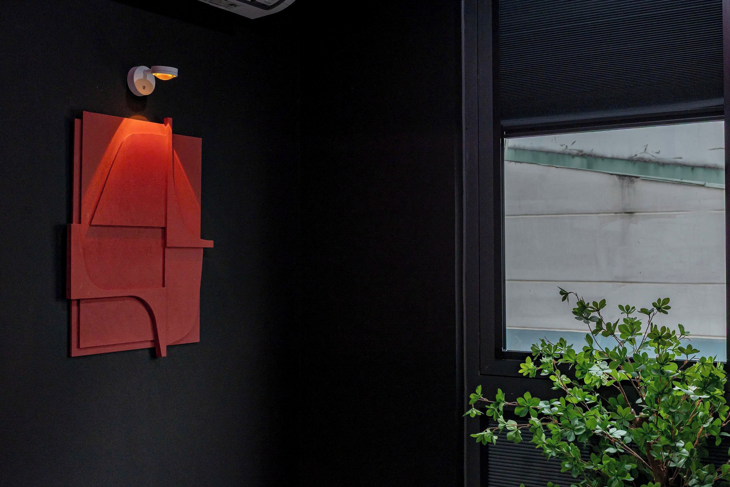 A modern wall-mounted light fixture with geometric shapes and a small plant beside a window.