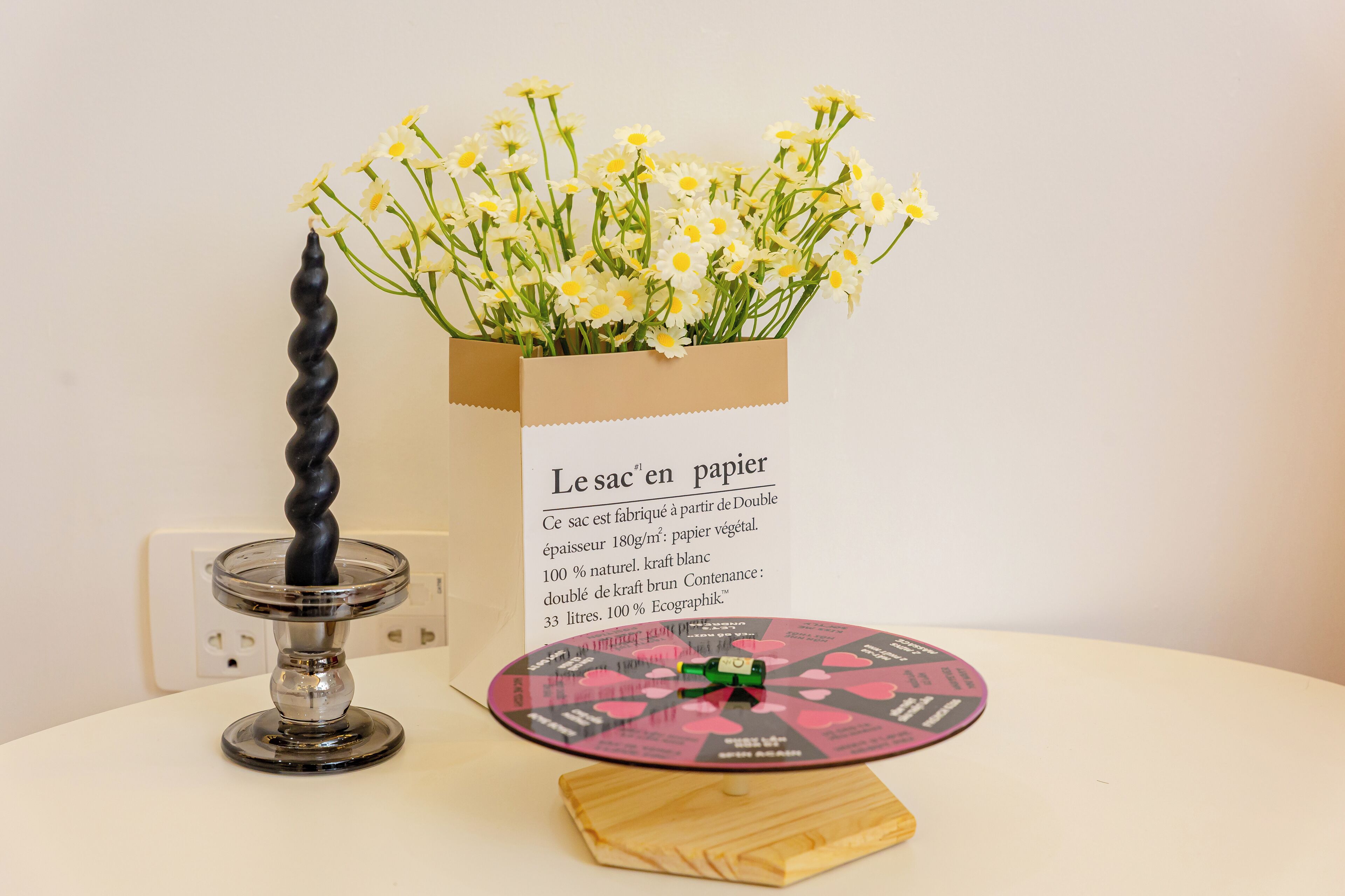 A table with a vase of flowers, a candle holder, and a card with text.