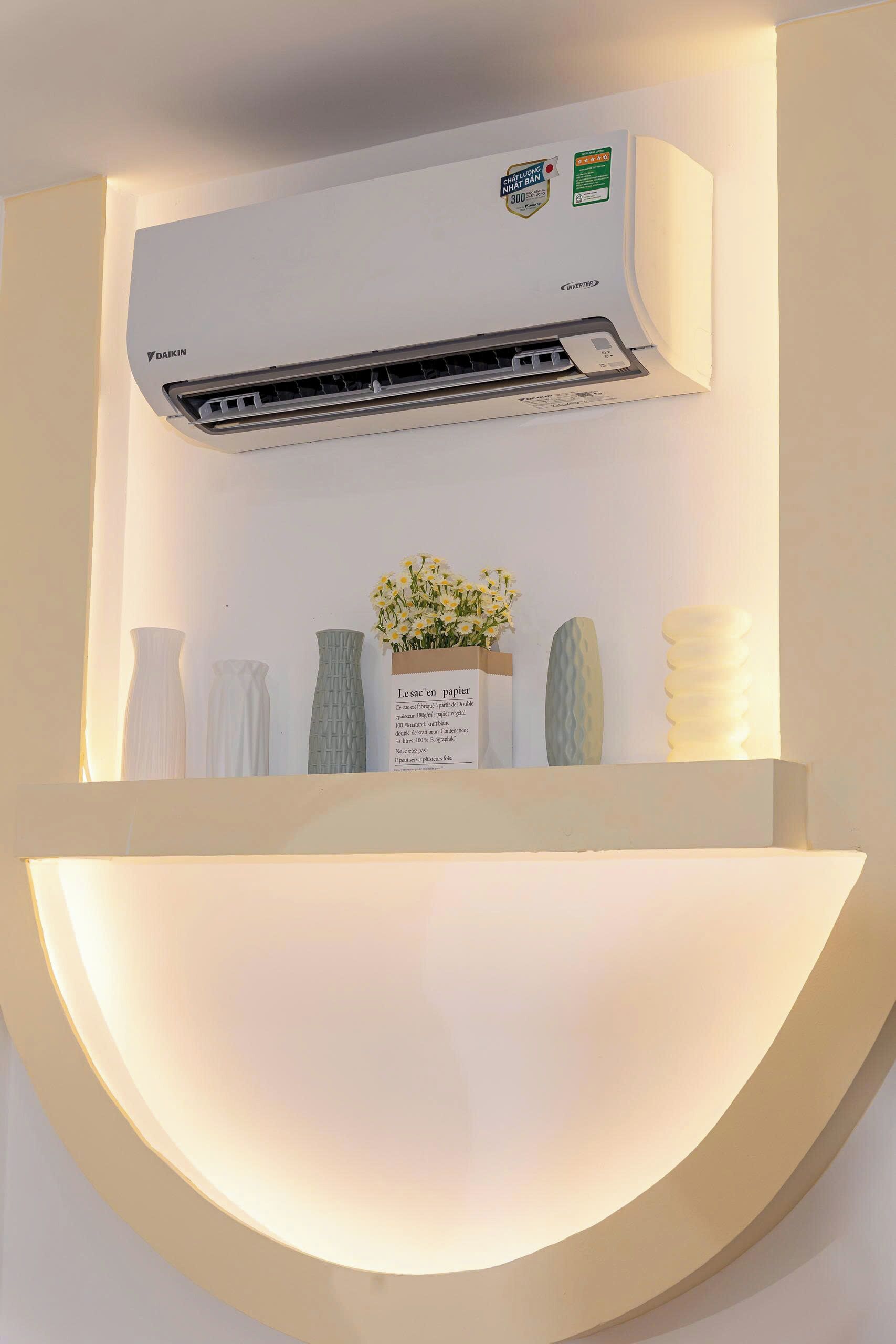 A wall-mounted air conditioner with a control panel, a shelf with decorative vases, and a sign with text.