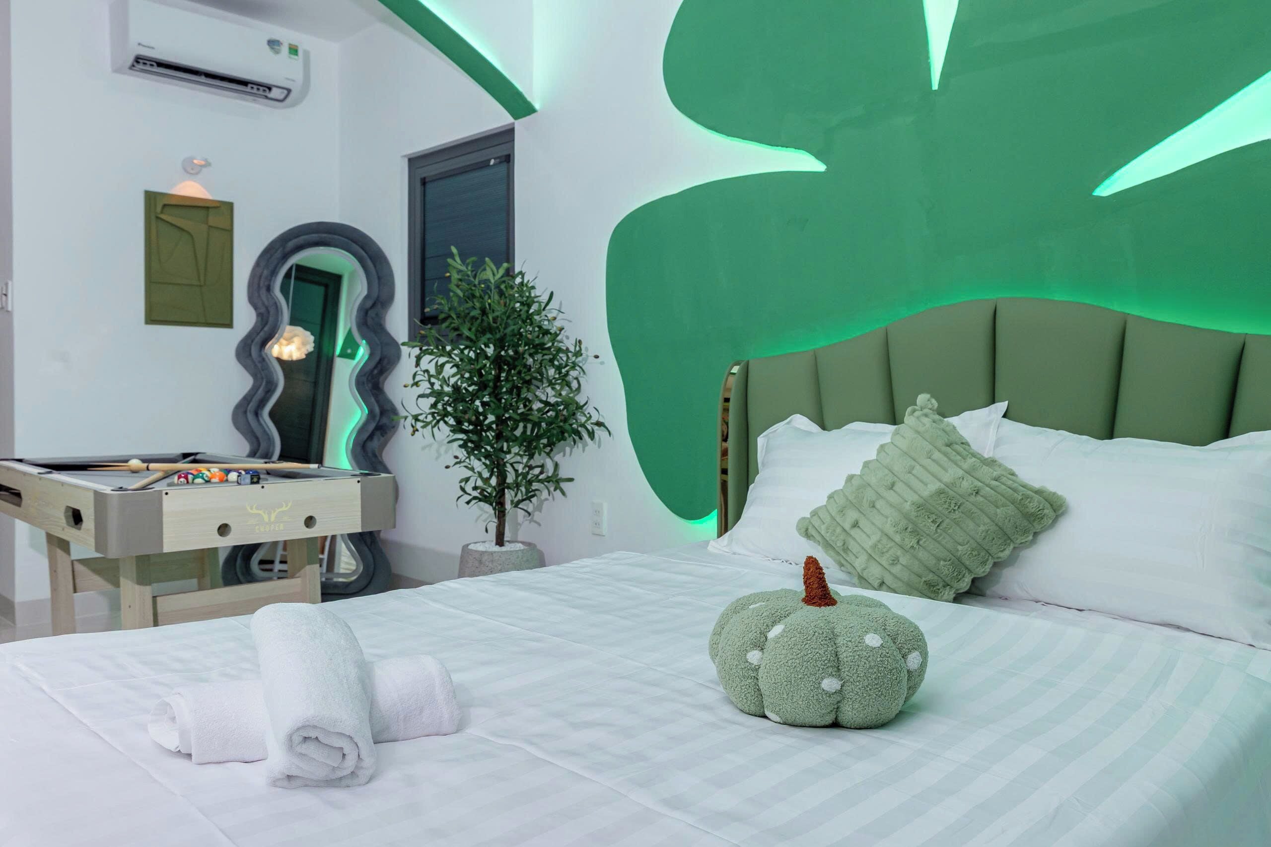 A hotel room with a bed, a massage table, a mirror, a potted plant, and a green wall design.