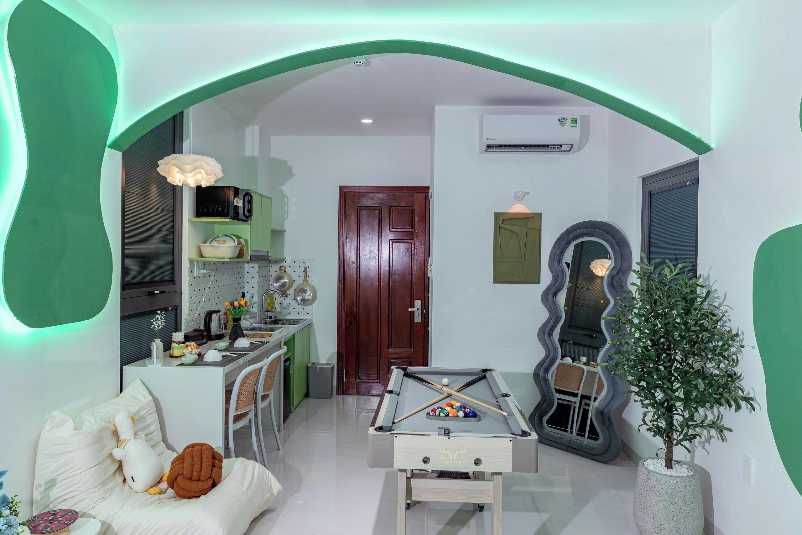A cozy living room with a pool table, a sofa with cushions, a small dining area, and a green-framed archway.