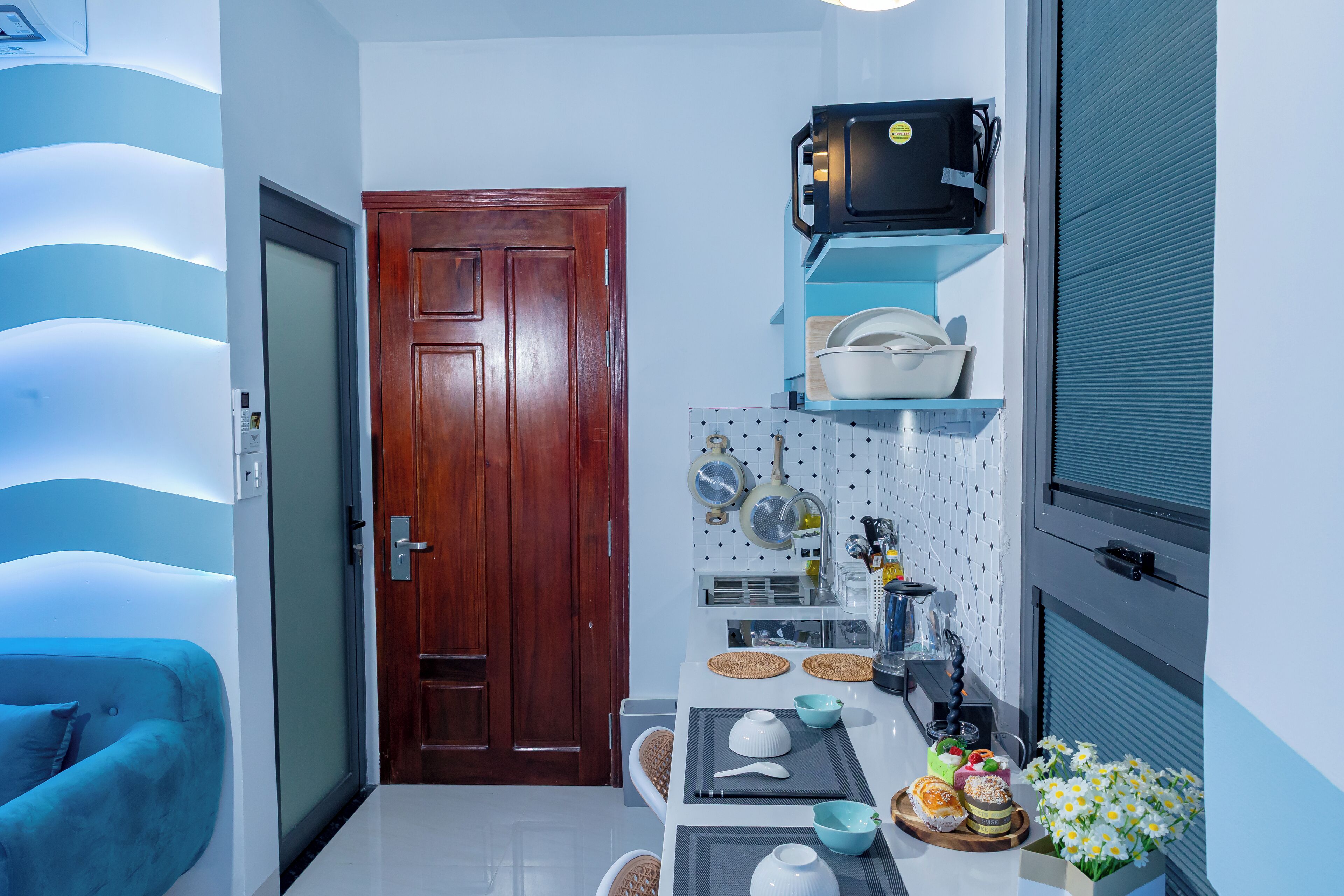 A compact kitchen with a wooden door, a microwave on a shelf, and a small dining area with a table set for two.