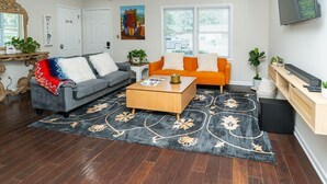 Un salon avec un canapé gris, un canapé orange, une table basse en bois et un grand tapis.
