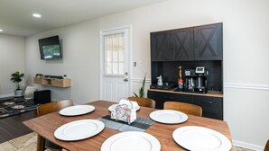 Un coin repas avec une table en bois dressée pour six personnes, une machine à café et un téléviseur fixé au mur.