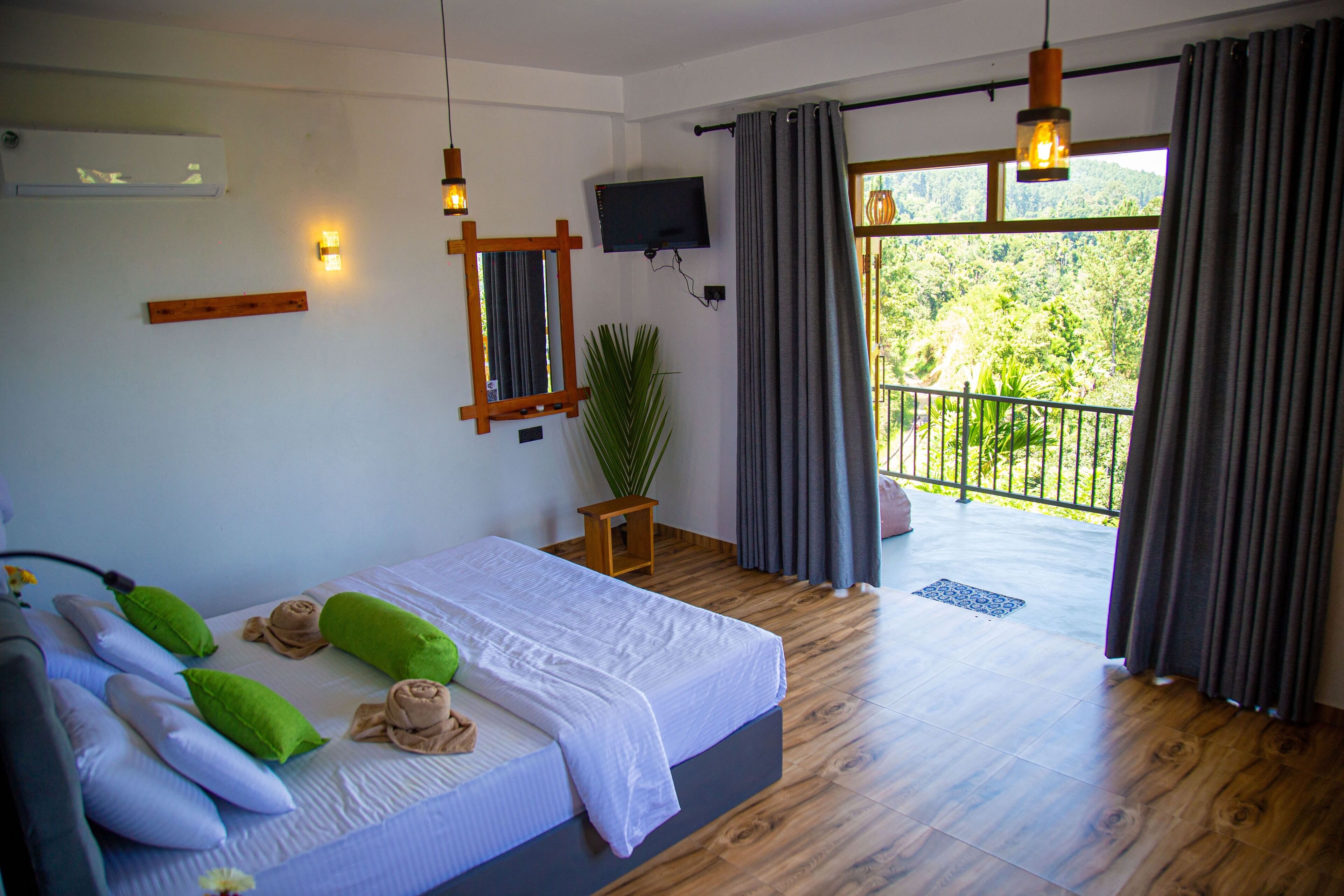 A bedroom with a bed, pillows, a TV, and a view of greenery outside.