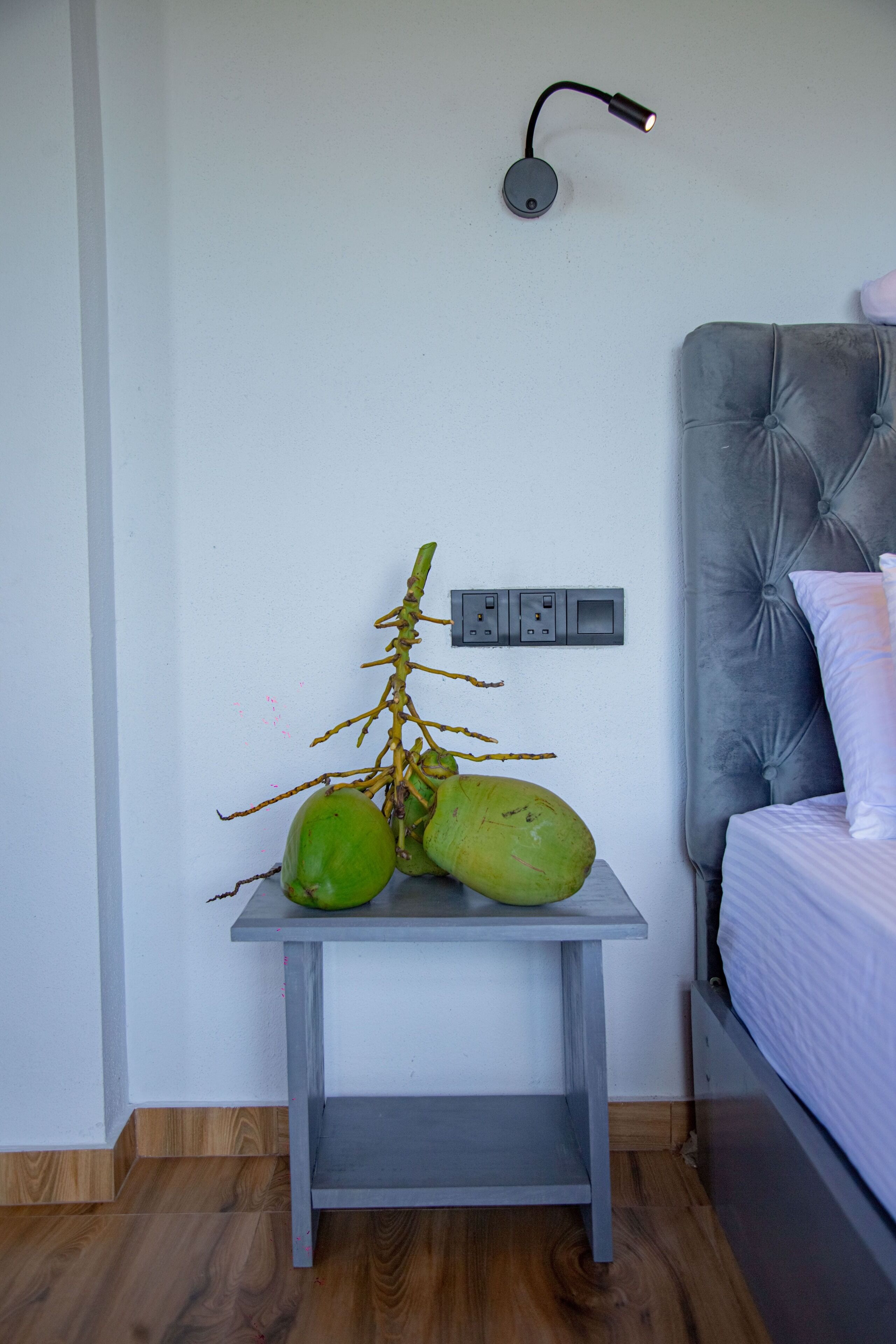A bedroom with a grey headboard, a bedside table with a lamp, and a wall socket.